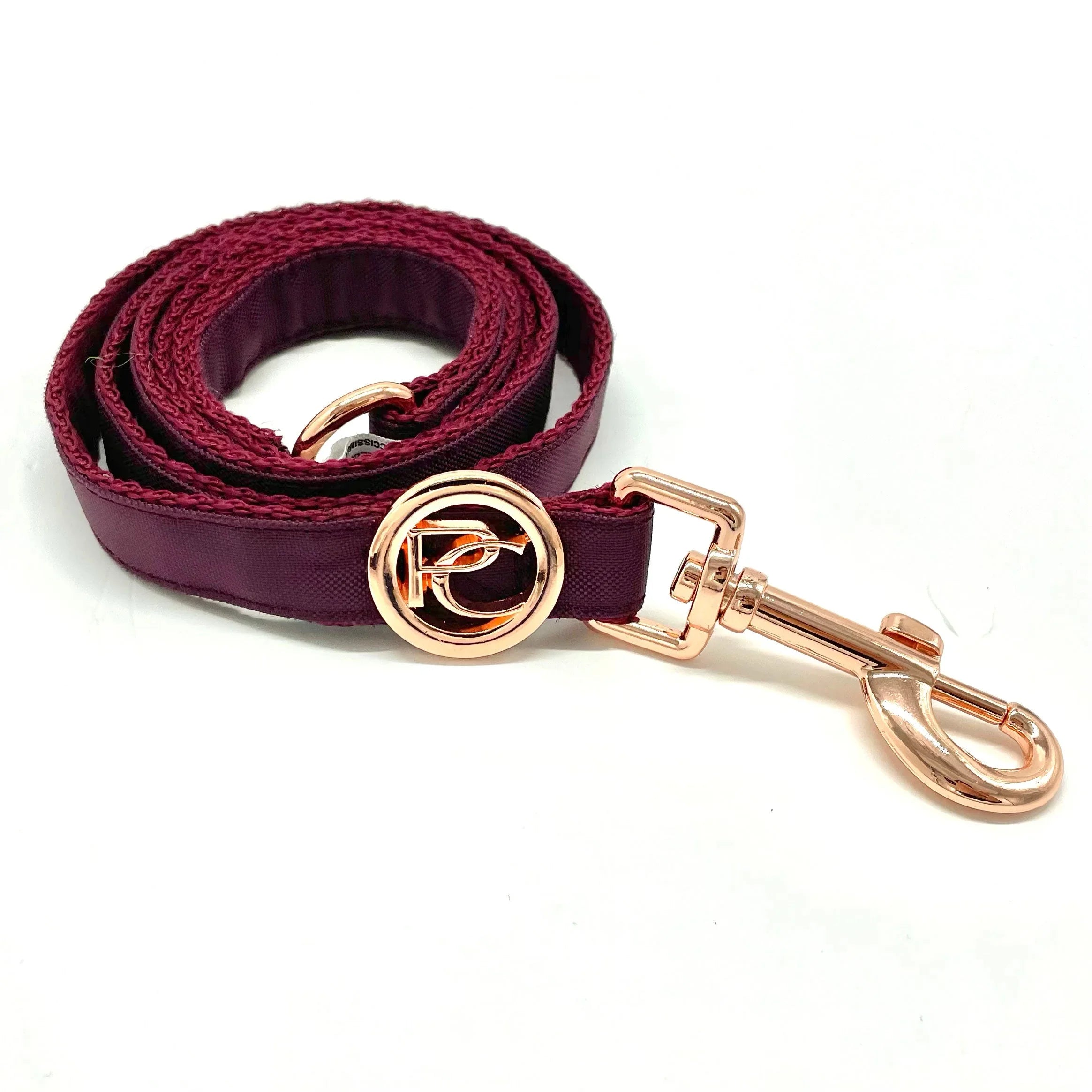 Burgundy dog leash with rose gold metal clasp and circular logo on white background