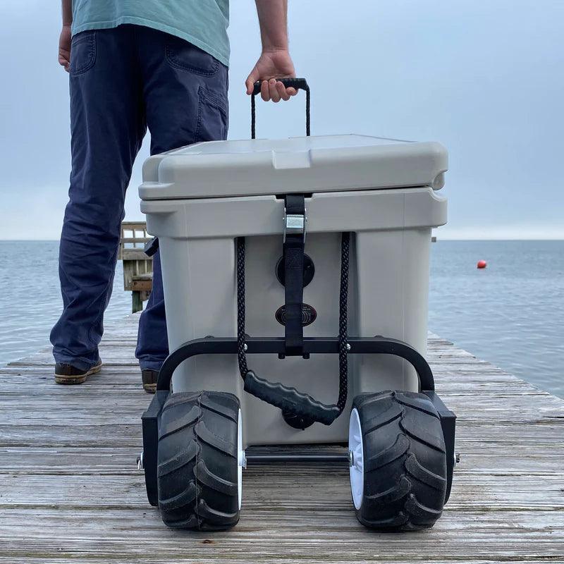 Man on dock pulling heavy-duty wheeled cooler near water, outdoor portable cooler