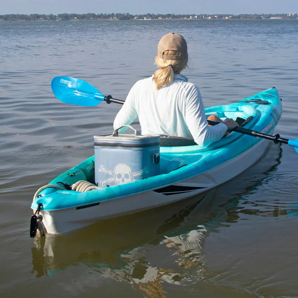 Person kayaking on a lake with a blue paddle and a skull-printed cooler in a turquoise kayak