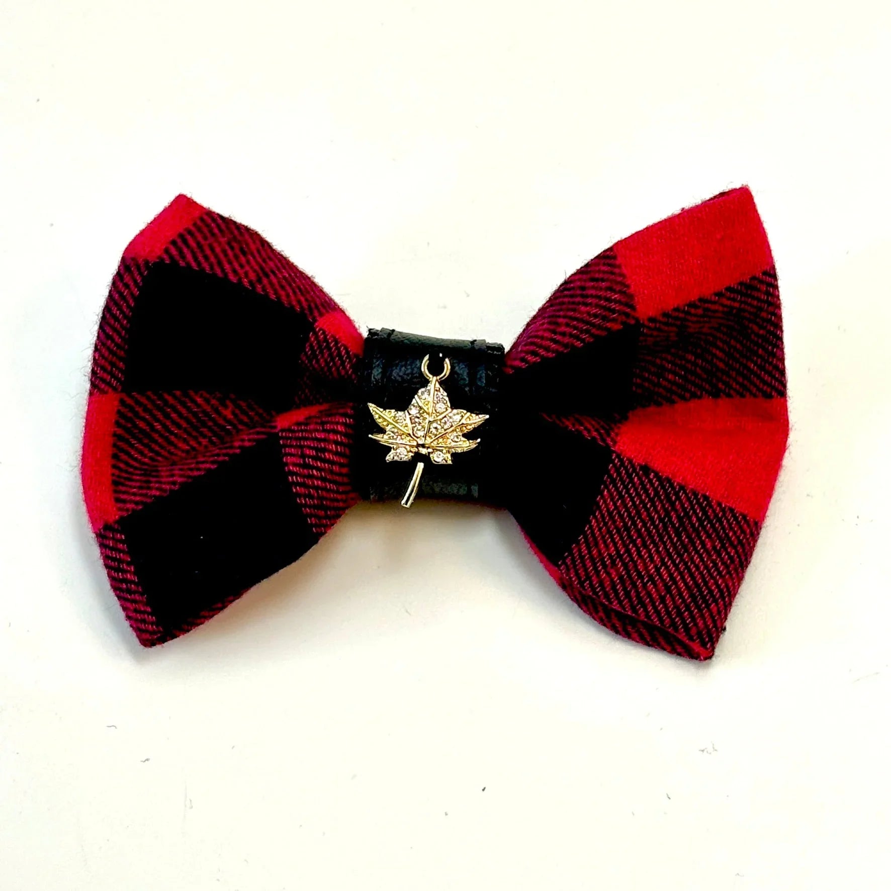 Red and black plaid bow tie with gold maple leaf charm on white background