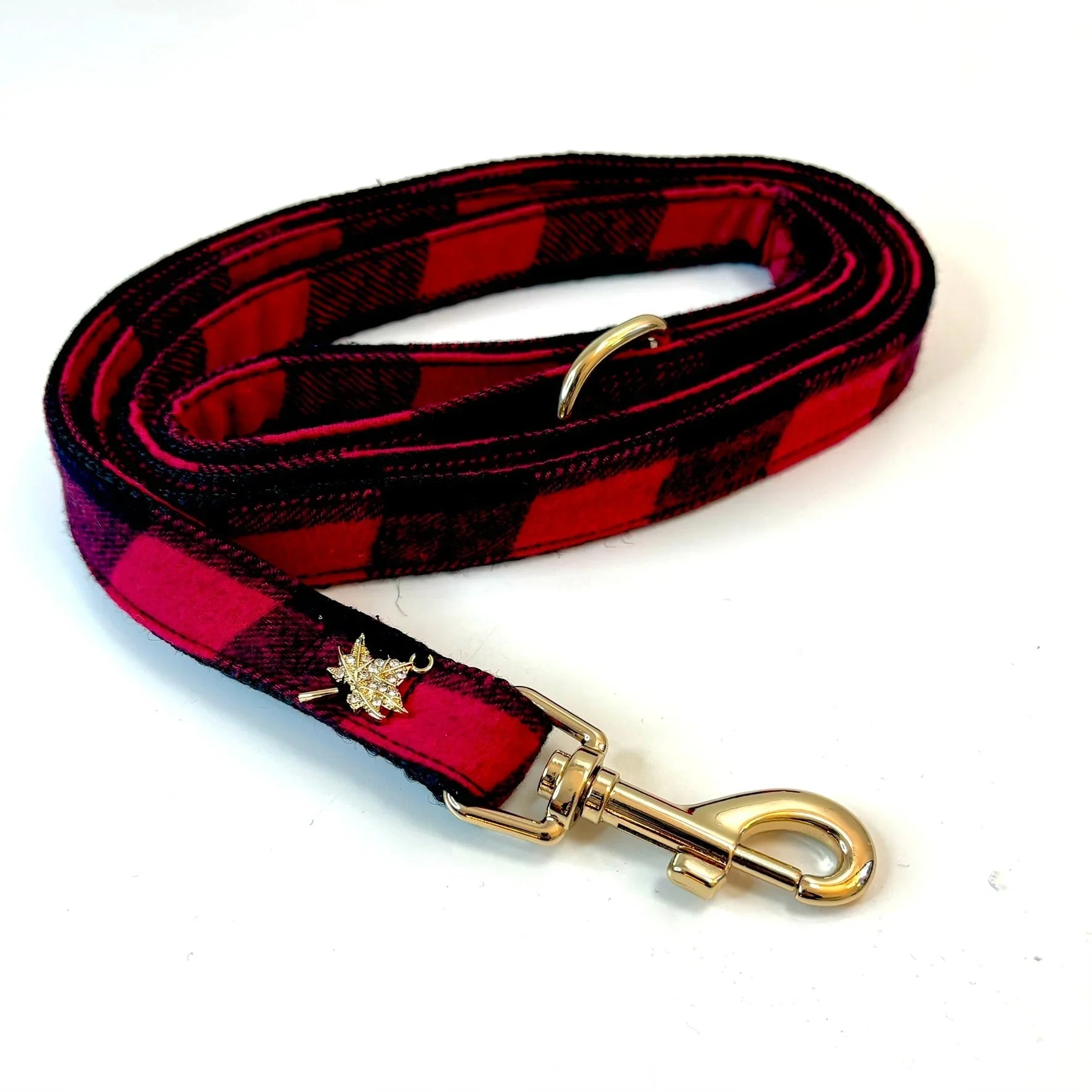 Red and black plaid dog leash with gold hardware and maple leaf charm on white background
