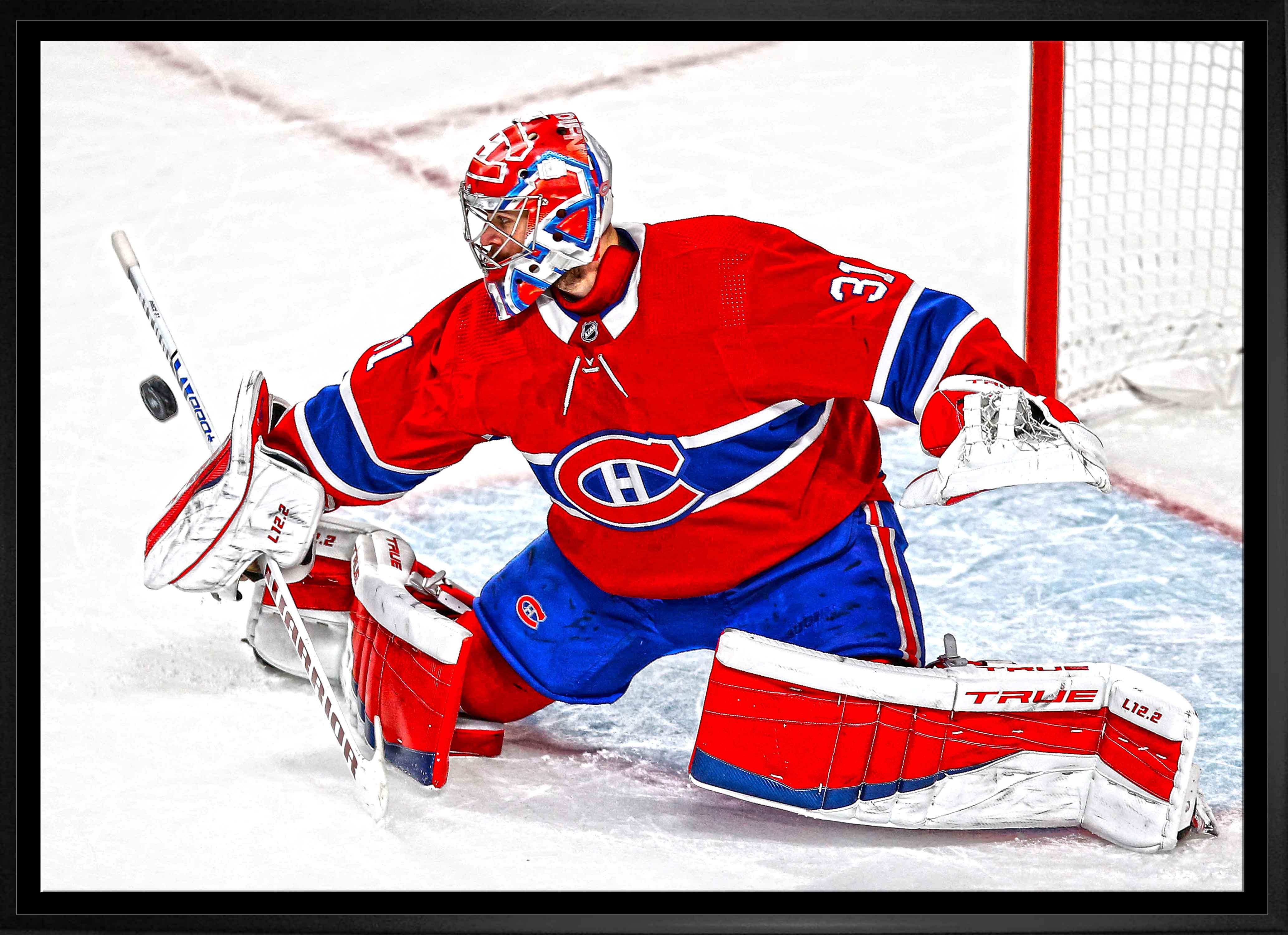 Montreal Canadiens goalie in red uniform blocking puck on ice hockey rink