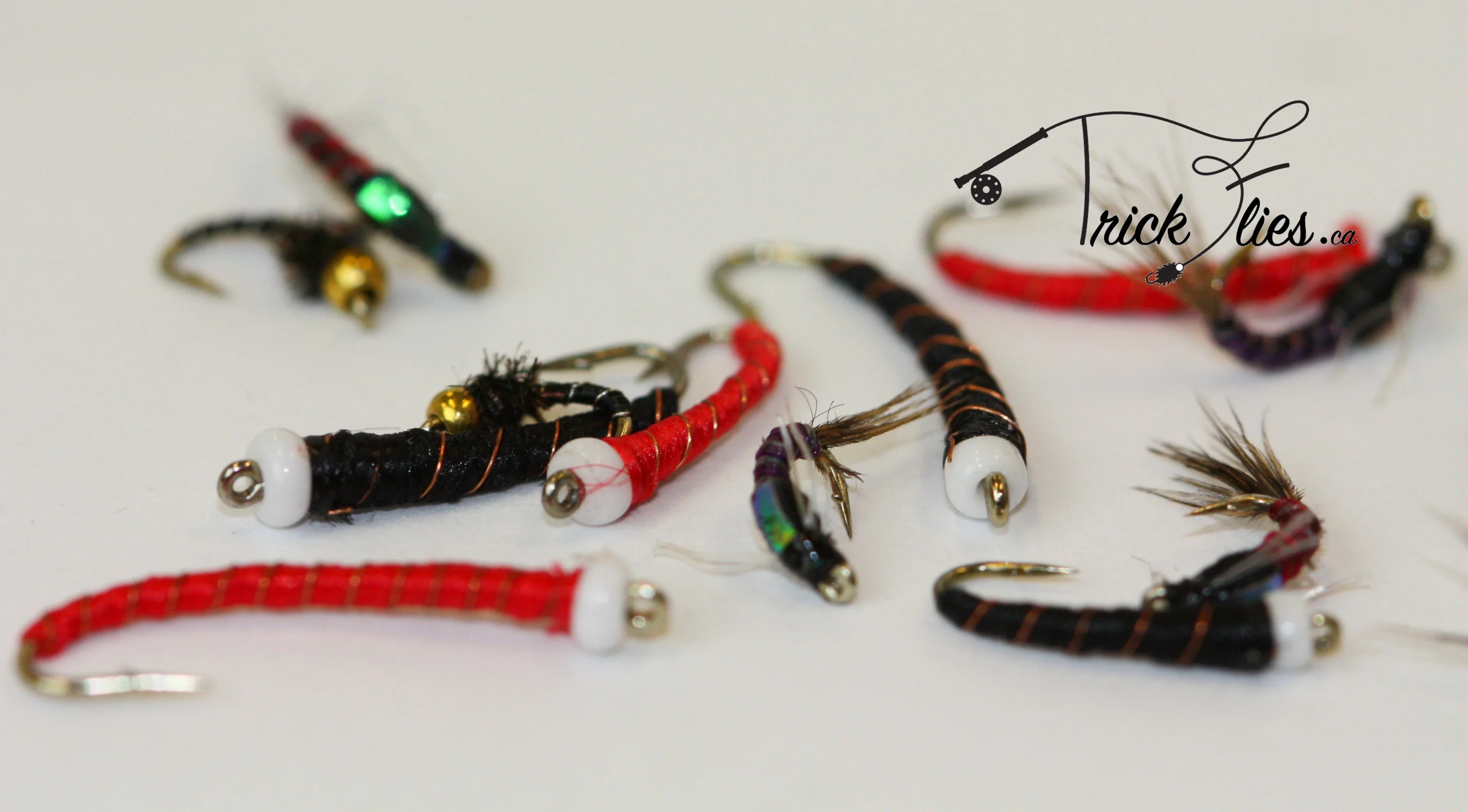 Assorted colorful fly fishing lures on white background, Trick Flies logo in corner.