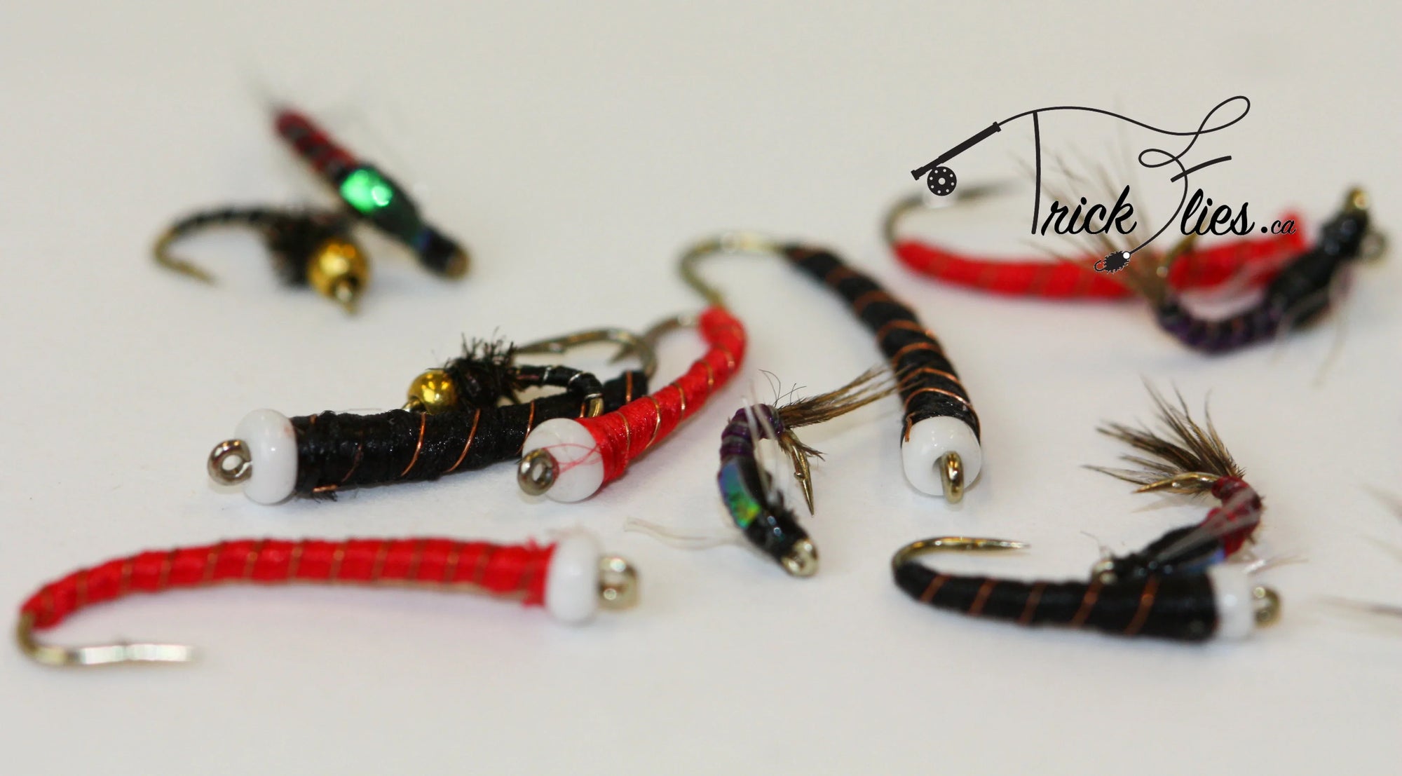 Assorted colorful fly fishing lures on white background, Trick Flies logo in corner.