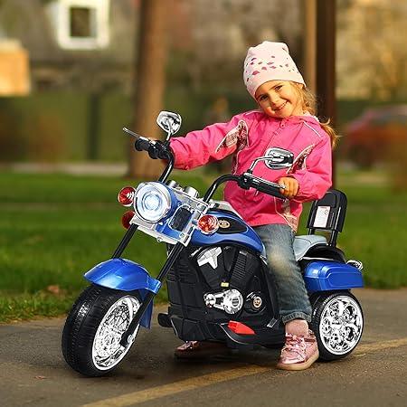 Smiling girl in pink jacket and hat riding blue toy motorcycle outdoors