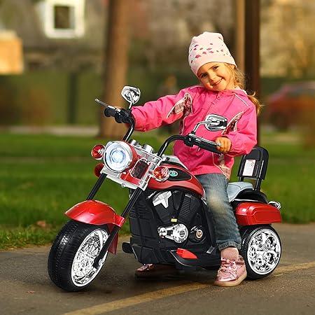 Smiling girl in pink jacket and hat riding red kids electric toy motorcycle outdoors