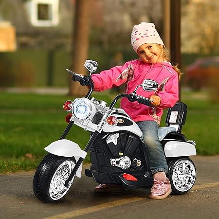 Smiling girl in pink jacket riding a white electric toy motorcycle outdoors