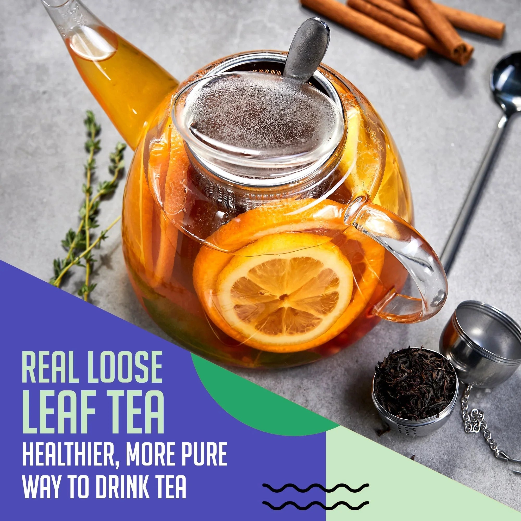 Glass teapot with loose leaf tea and citrus slices on gray table, cinnamon sticks, fresh herbs.