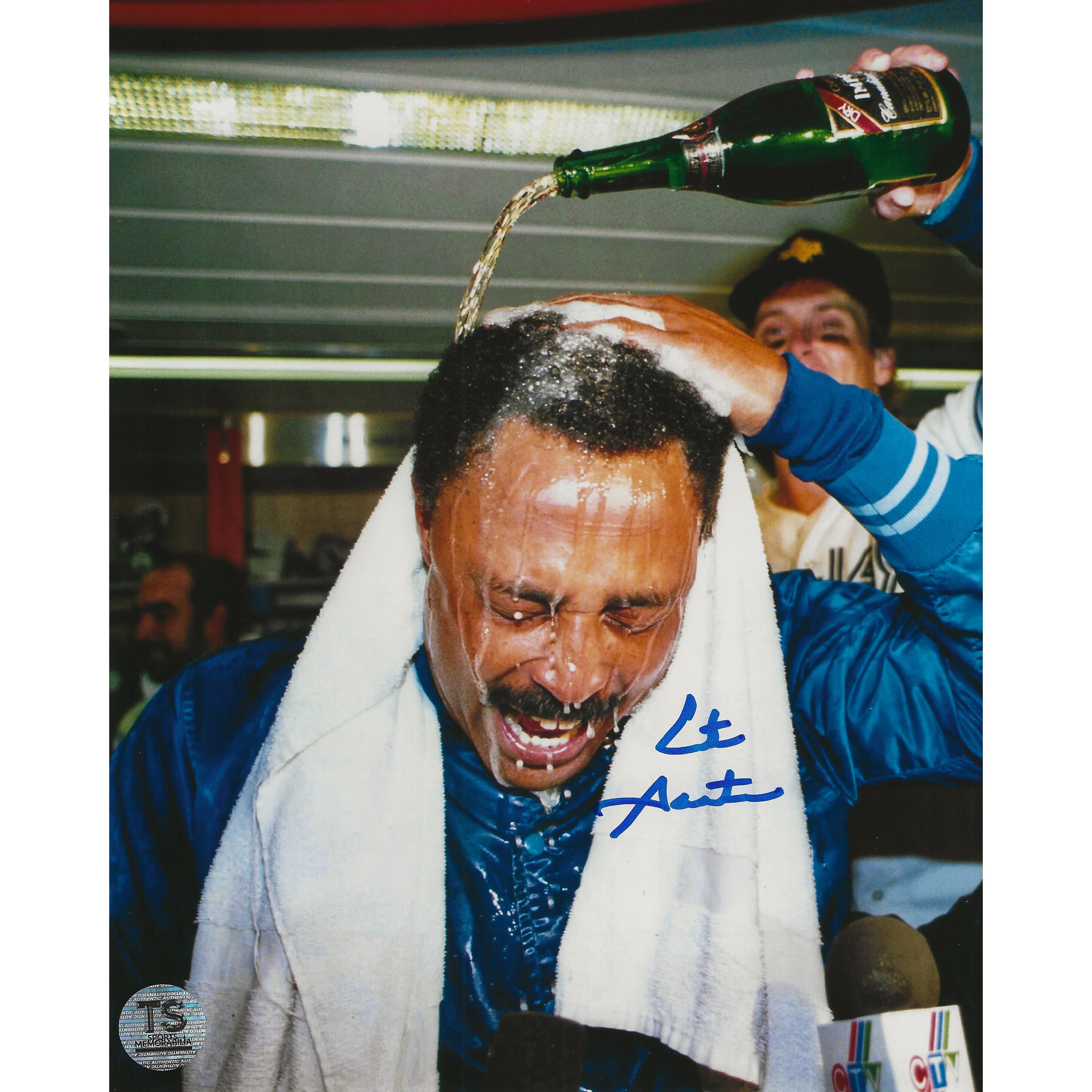 Man in blue jacket celebrating with champagne poured on head, wearing white towel, smiling