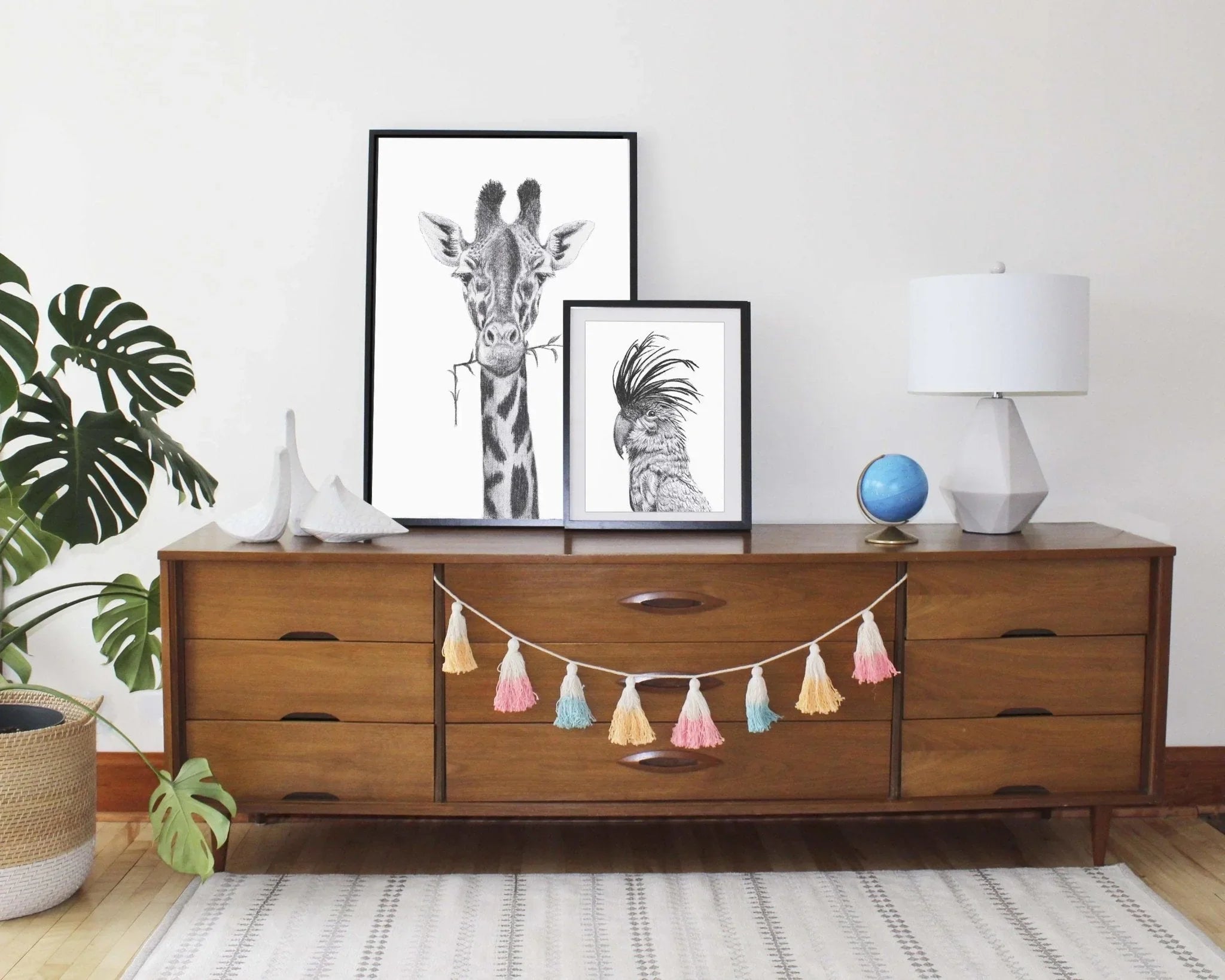 Framed cockatoo portrait and giraffe artwork on mid-century wooden dresser in modern room