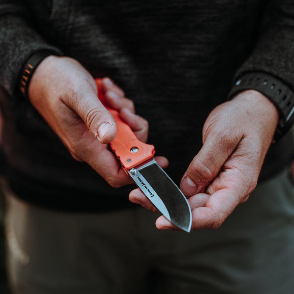 Man holding Ultimate Hunter folding knife with orange handle outdoors