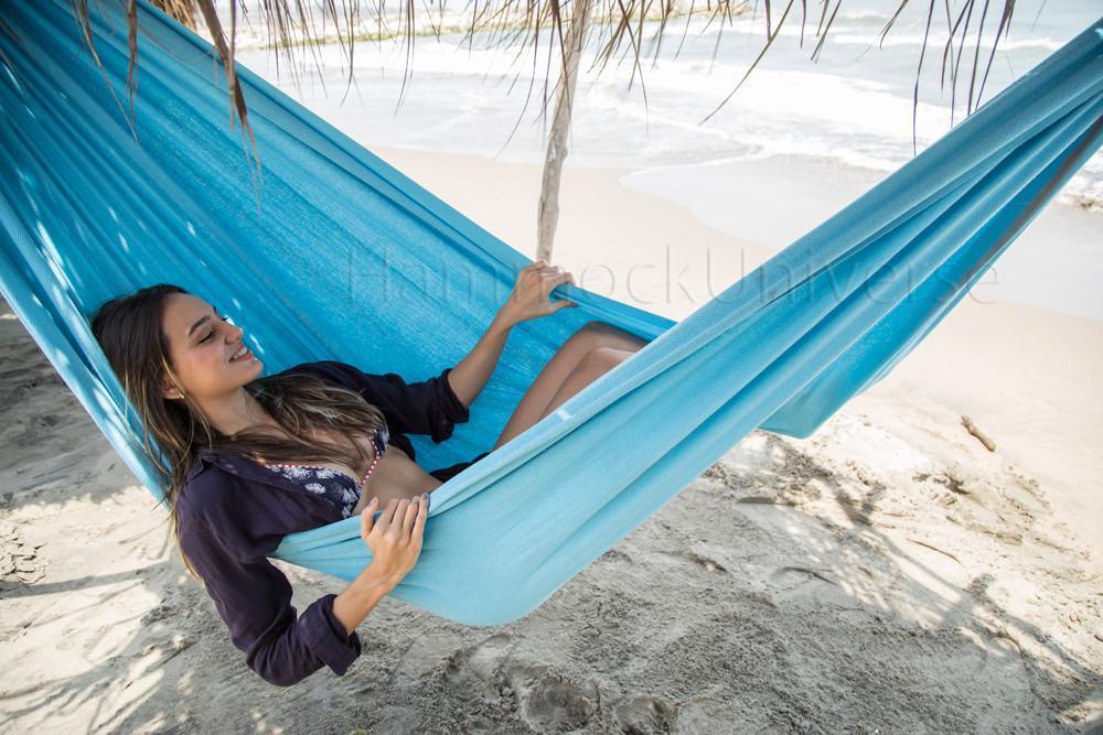 Woman relaxing in blue Colombian hammock on tropical beach under palm shade