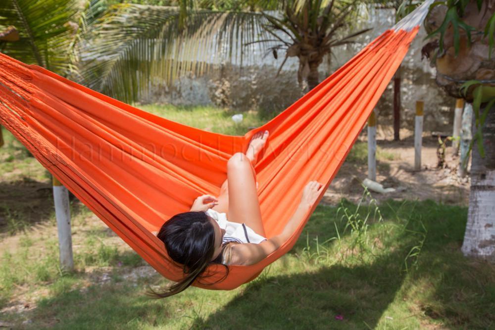 Woman relaxing in an orange Colombian hammock outdoors near palm trees and grass
