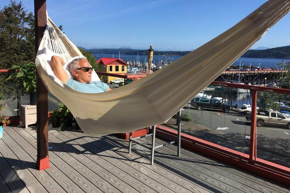 Man relaxing in a natural Colombian double hammock on a wooden deck overlooking a marina