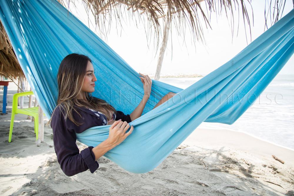 Woman relaxing in a blue Colombian hammock on a sandy beach under palm shade by the ocean