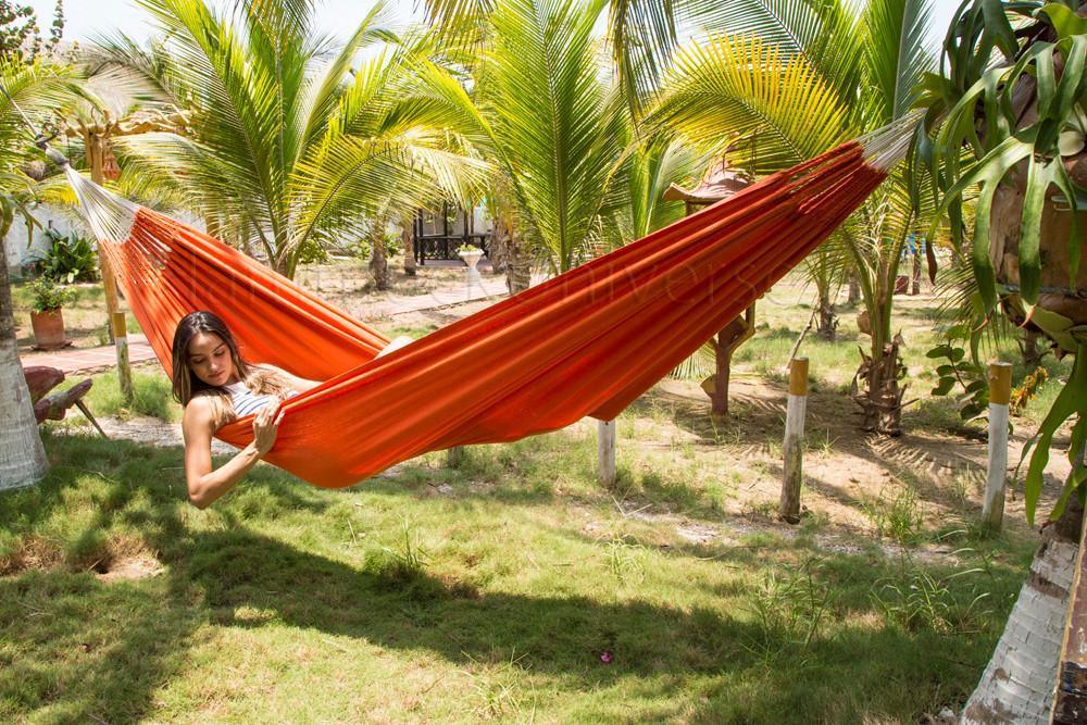 Woman relaxing in an orange Colombian hammock outdoors among palm trees