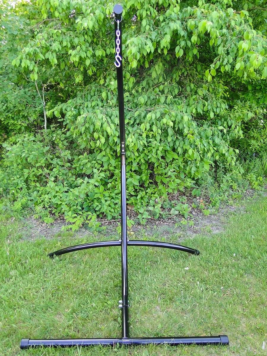 Black metal hammock chair stand outdoors on green grass with leafy bushes behind