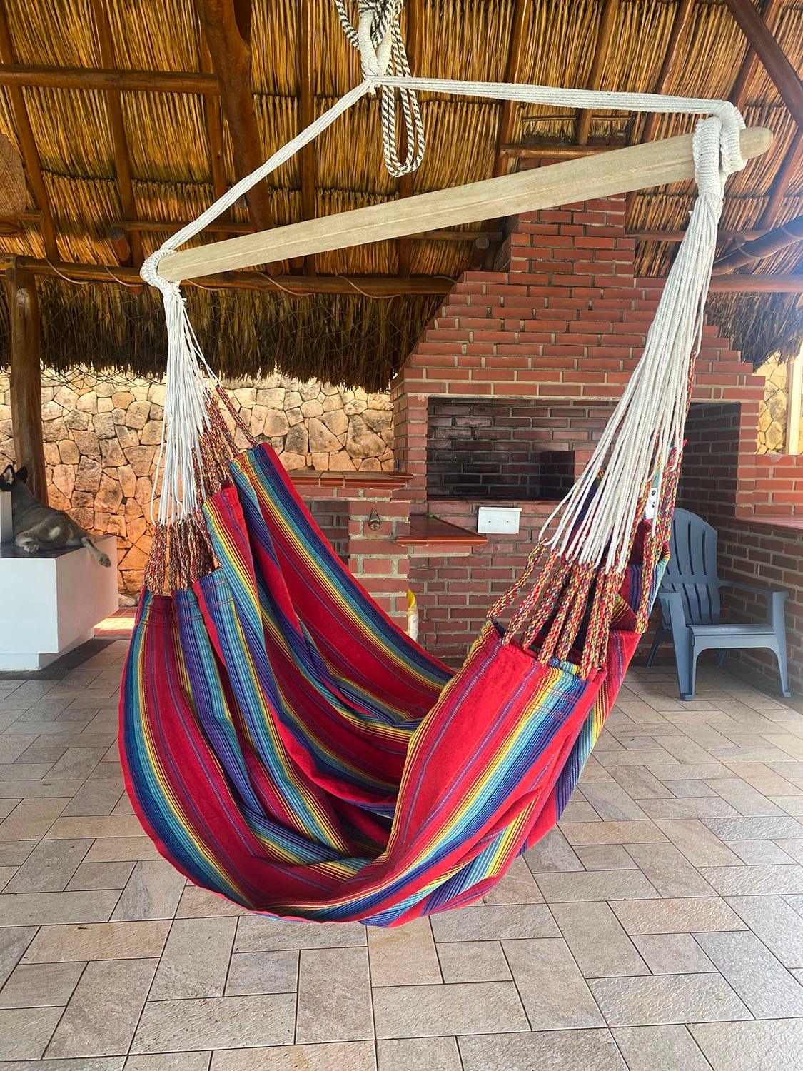 Colorful hammock chair with striped fabric hanging under a thatched patio roof