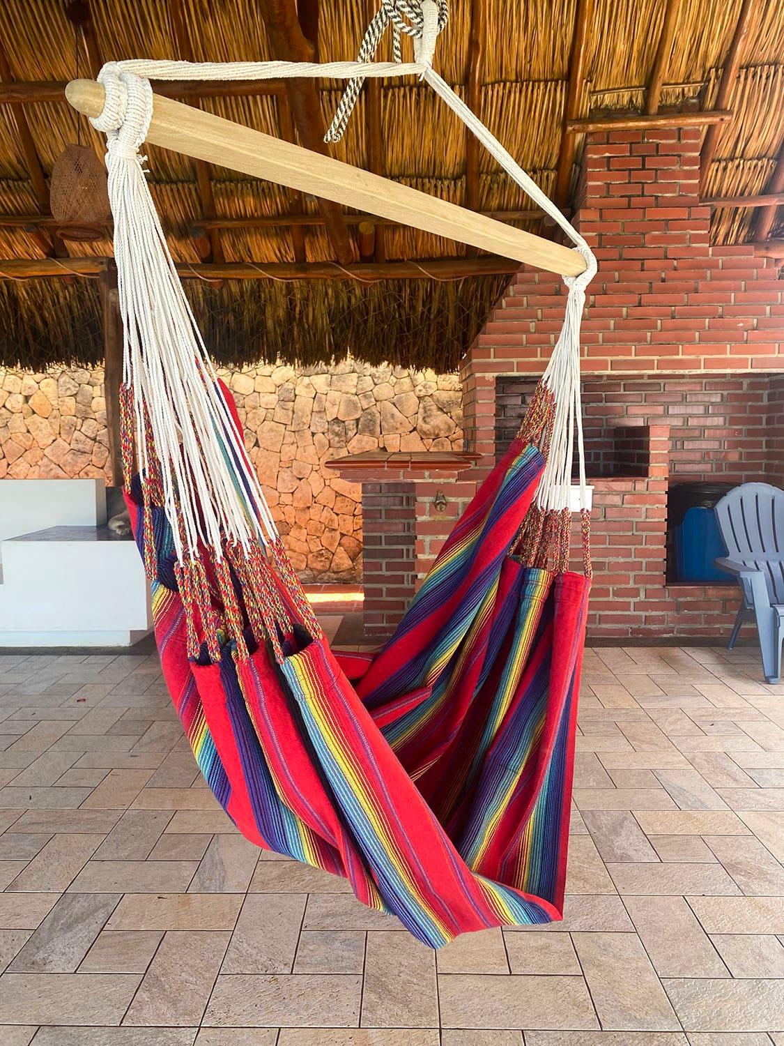 Colorful hammock chair with wooden spreader in a patio with brick grill and thatched roof