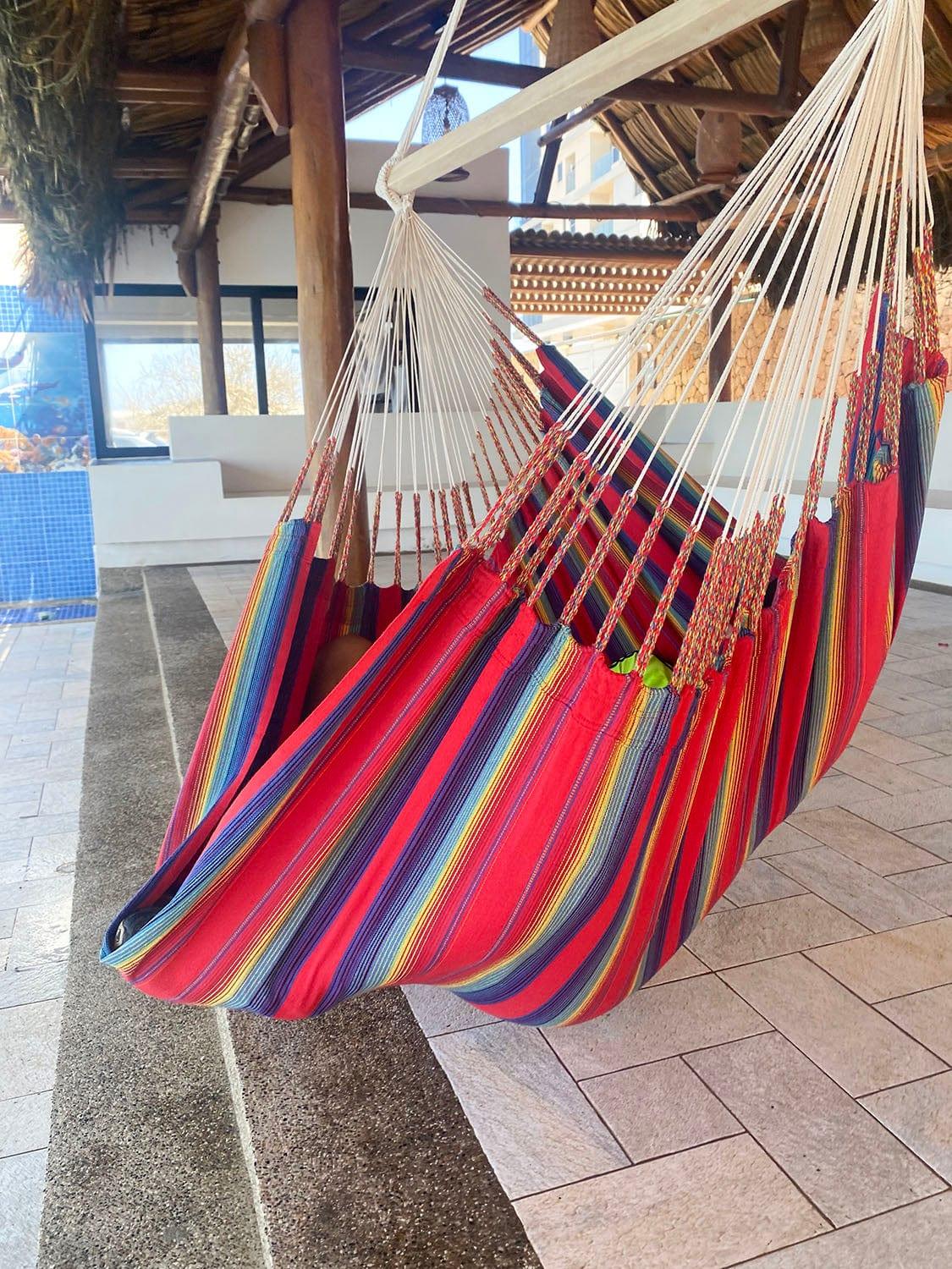 Colorful striped hammock chair hanging indoors under a thatched roof patio