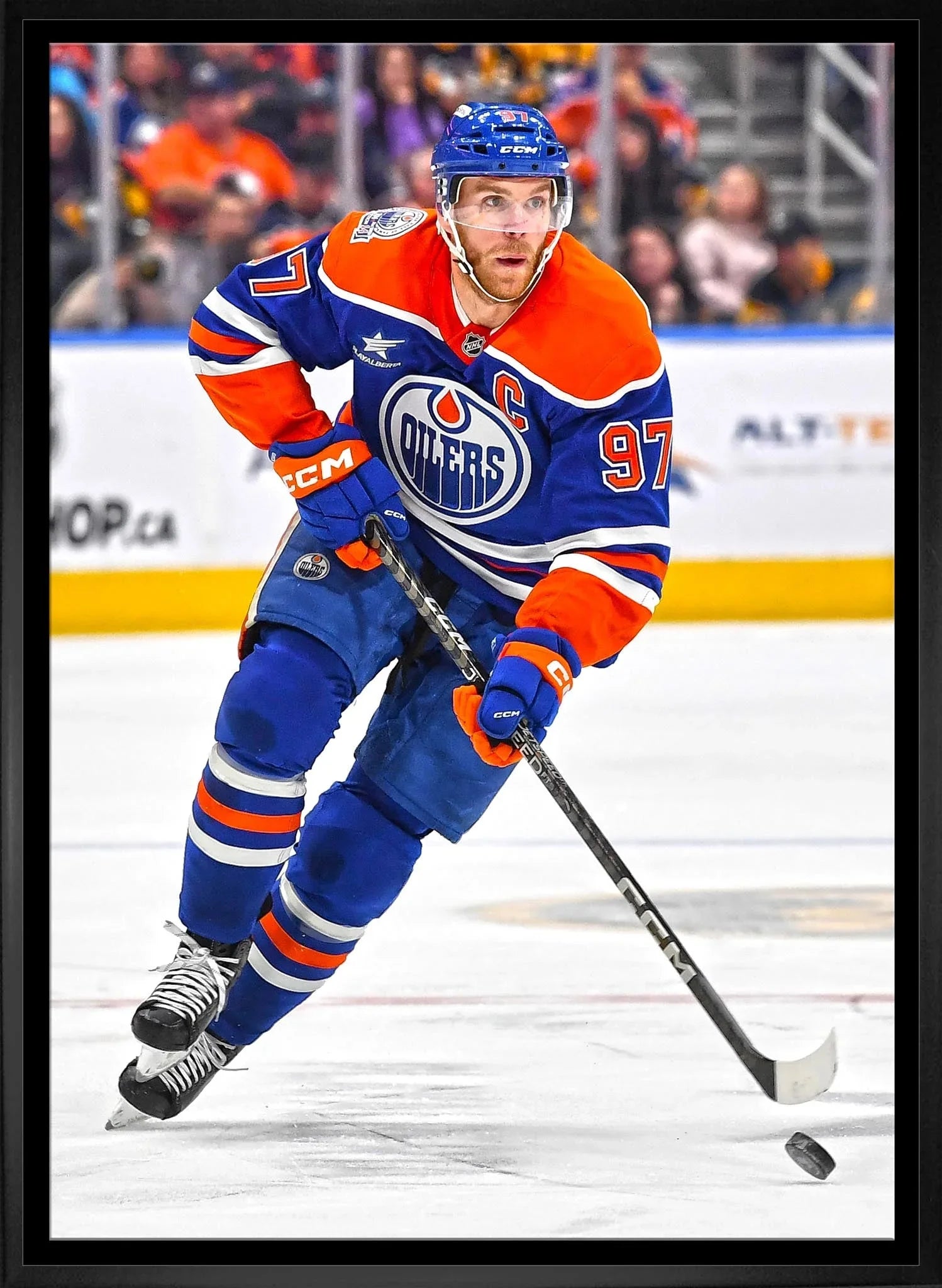 Edmonton Oilers hockey player in blue and orange uniform skating on ice with puck
