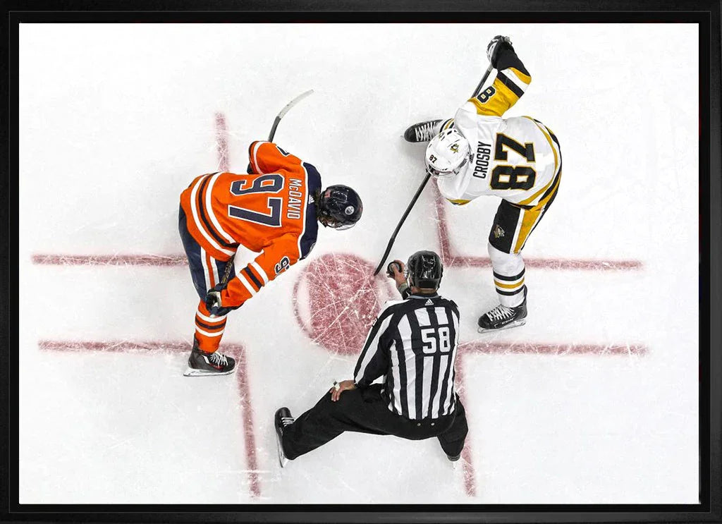 Two NHL hockey players face off on the ice with a referee at center ice, top view.