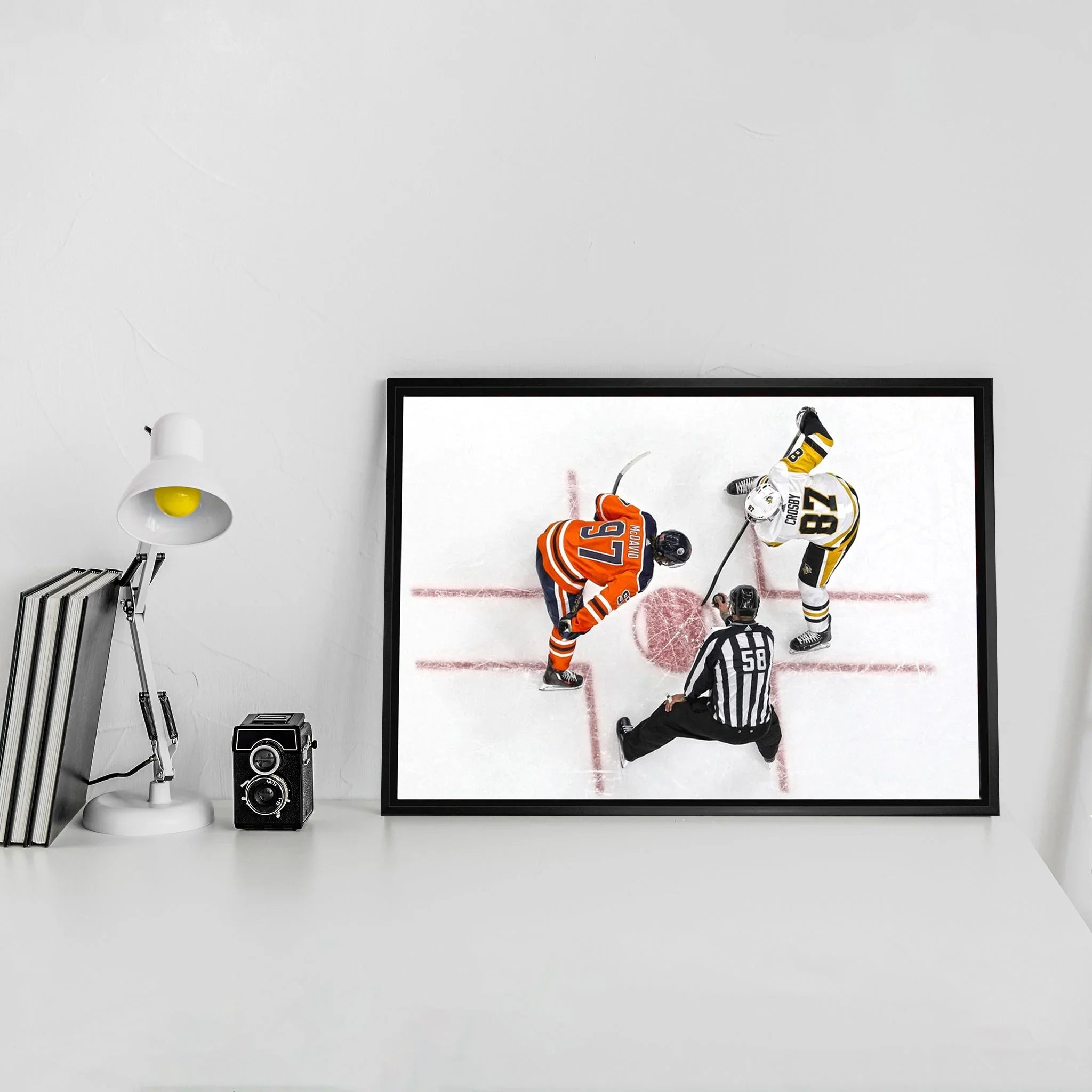 Framed hockey faceoff photo on modern white desk with books, lamp, and vintage camera