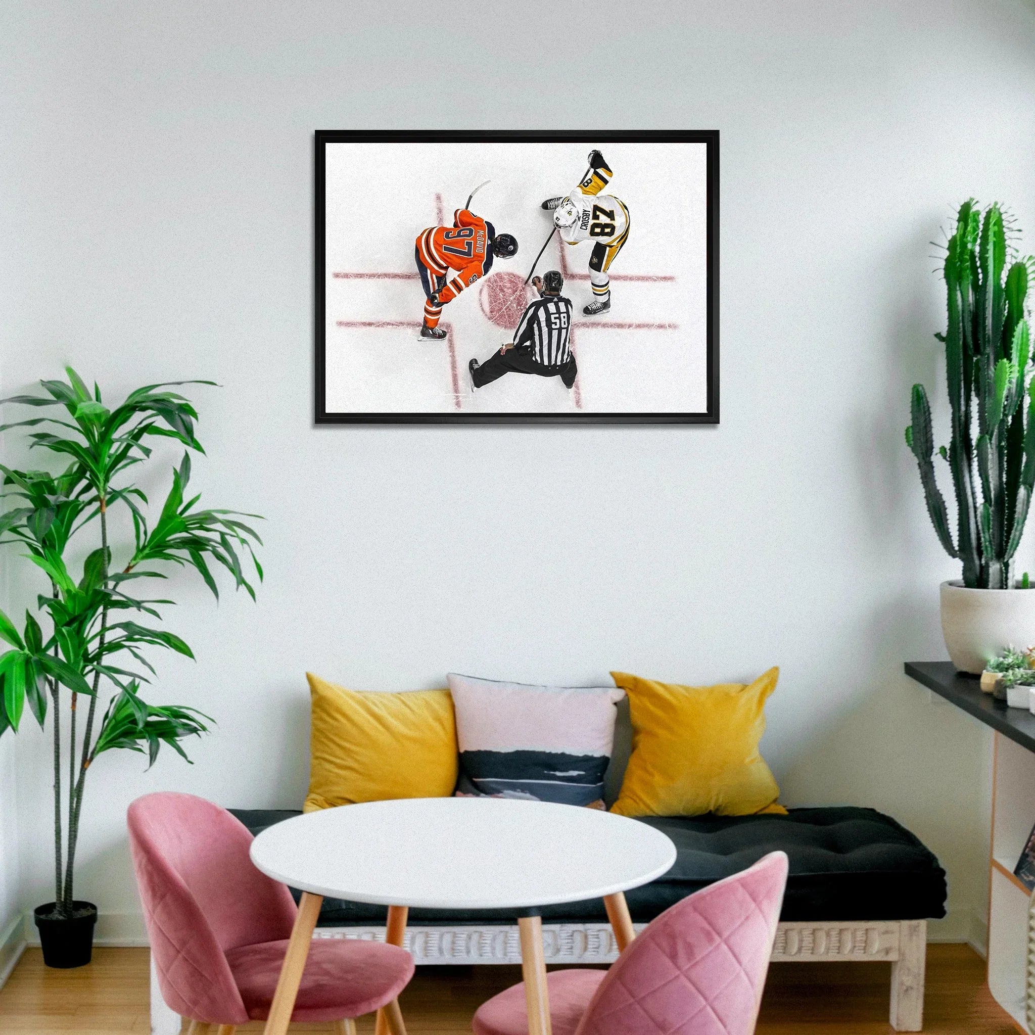 Modern living room with hockey-themed wall art, pink chairs, white table, plants, and pillows.