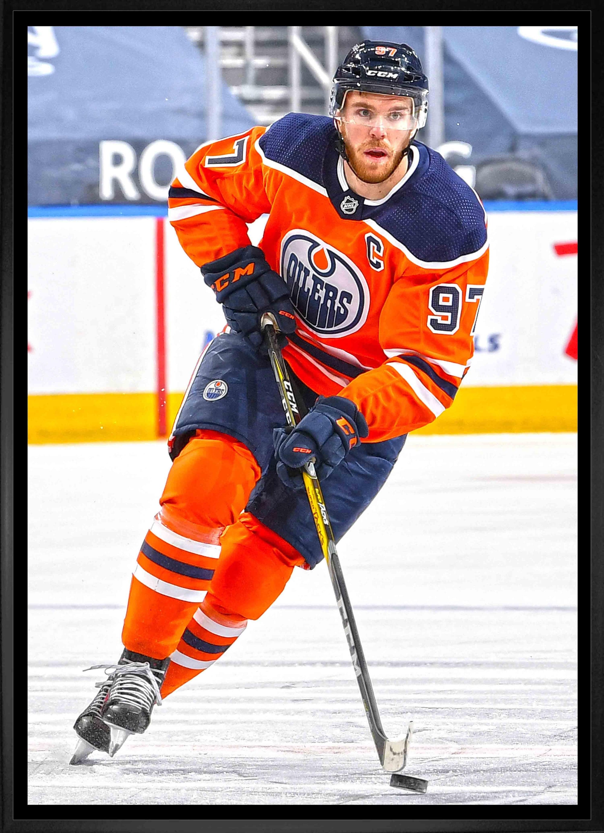 Edmonton Oilers hockey player in orange jersey skating with stick on ice rink