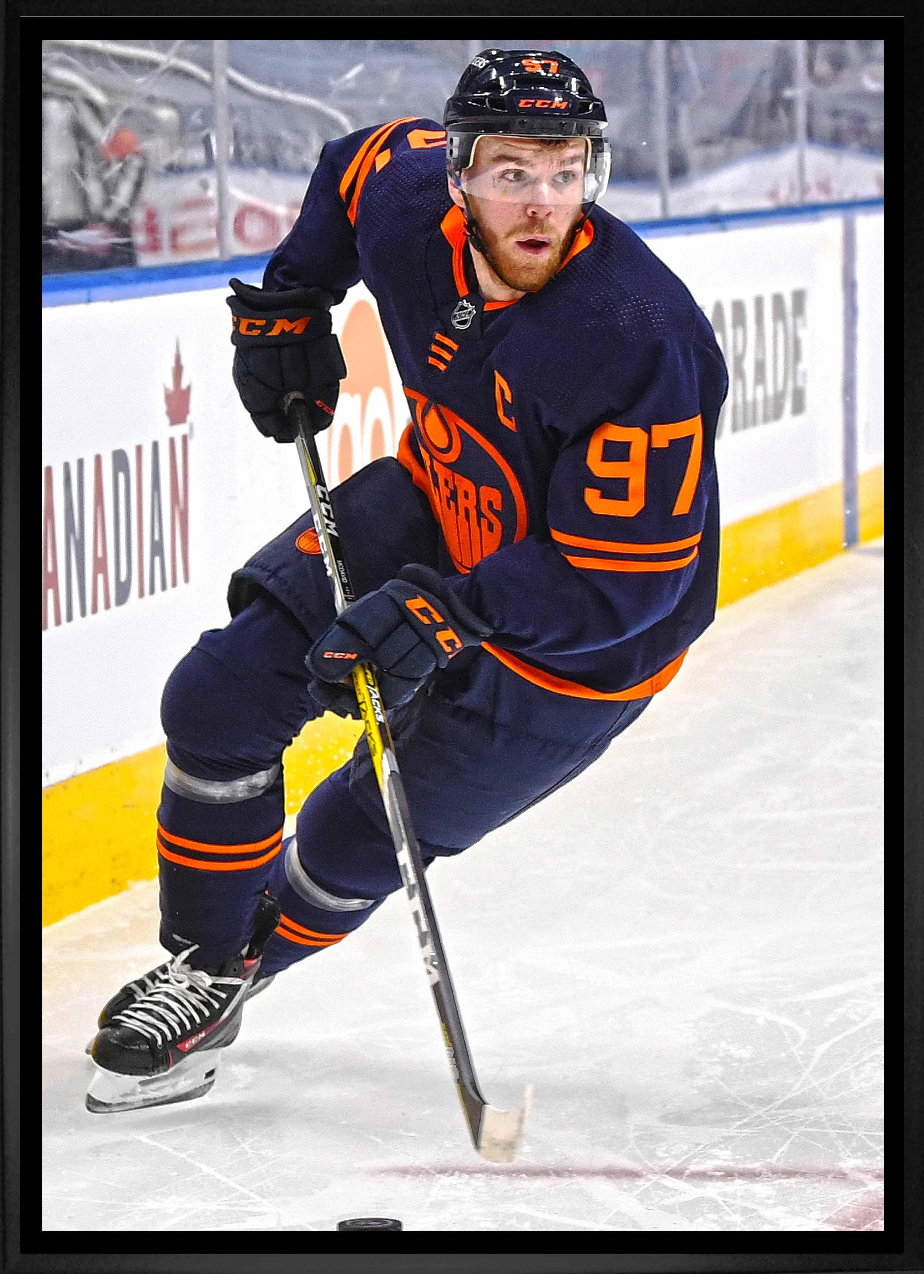 Hockey player in blue Edmonton Oilers jersey skating on ice rink with stick