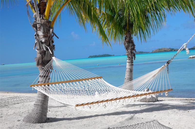 Double cotton rope hammock between palm trees on a tropical beach with turquoise ocean