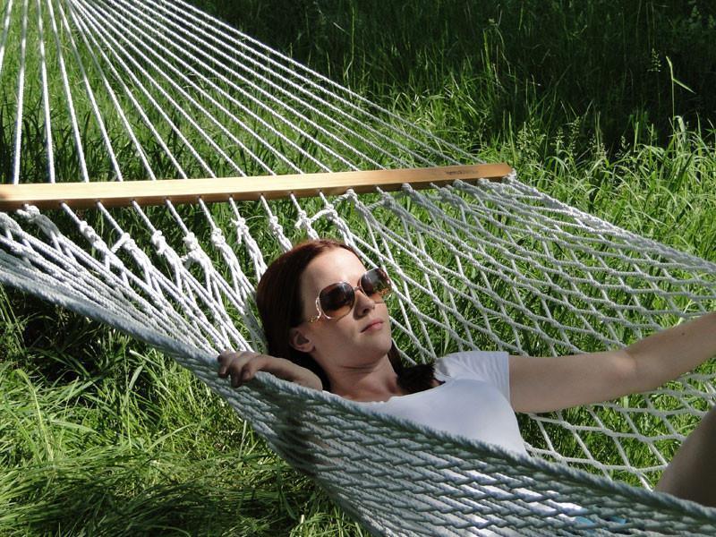 Woman relaxing on cotton rope hammock outdoors in green grassy yard