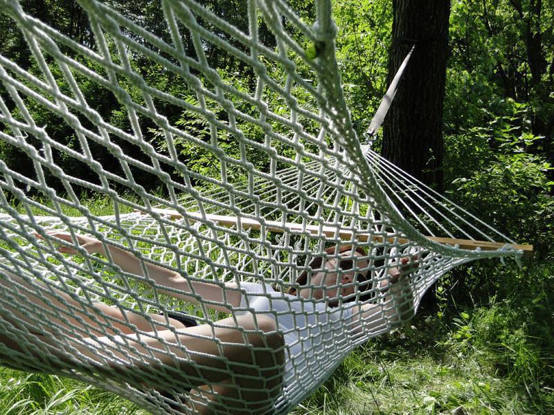 Person relaxing in a white cotton rope hammock outdoors among green trees and grass