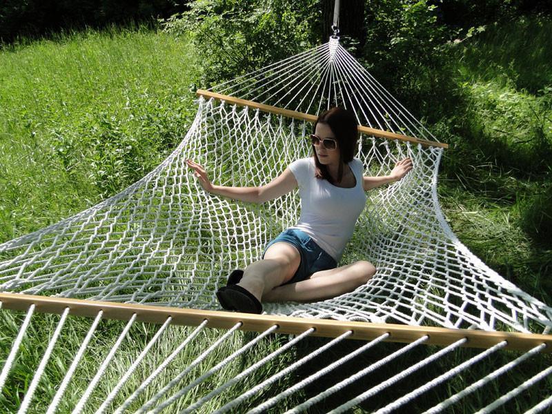 Woman relaxing on a white cotton rope hammock outdoors in a grassy yard
