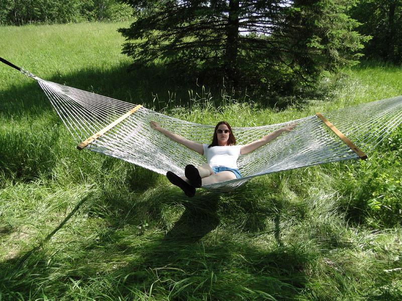 Woman relaxing on cotton rope hammock in grassy outdoor setting with trees