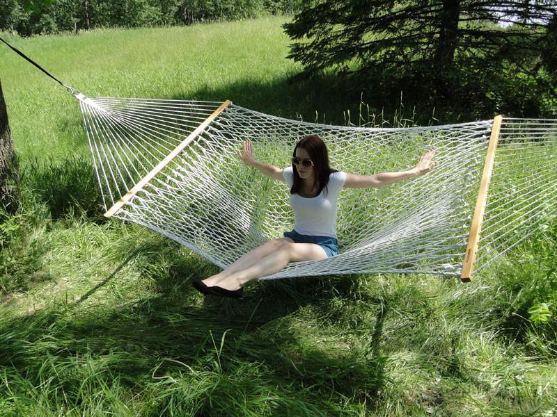 Woman relaxing on white cotton rope hammock outdoors in a grassy, sunny yard