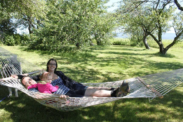 Family relaxing on cotton rope hammock outdoors under trees on a sunny day
