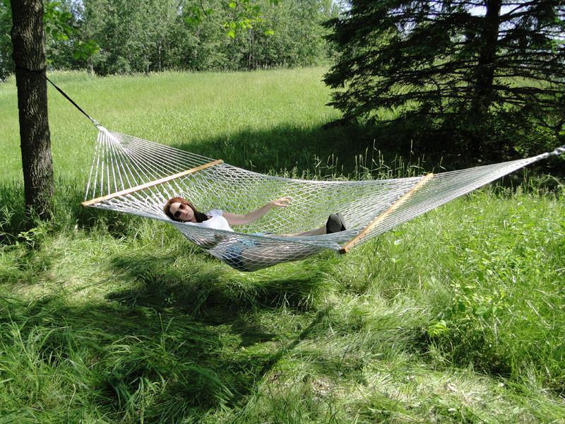 Woman relaxing in a cotton rope hammock outdoors in a grassy, wooded area