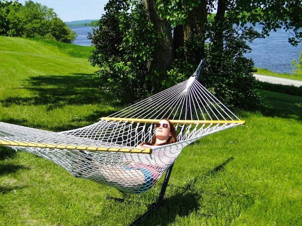 Woman relaxing on a cotton rope hammock with metal stand in a sunny lakeside backyard