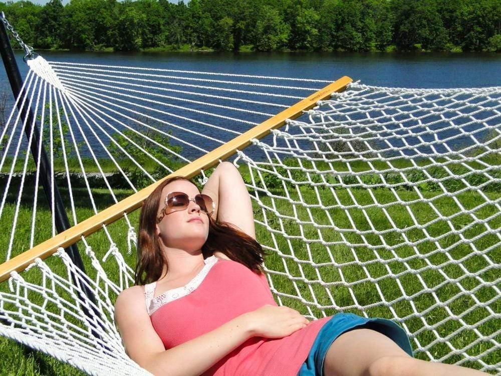 Woman relaxing on a 15-foot cotton rope hammock by a lake in a grassy outdoor setting