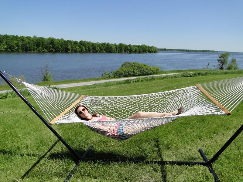 Woman relaxing in cotton rope hammock on tri-beam stand by lake on grassy lawn