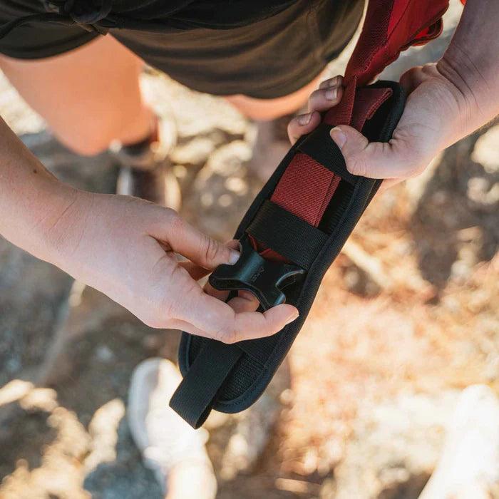 Person adjusting a black and red backpacker holster outdoors on a hiking trail