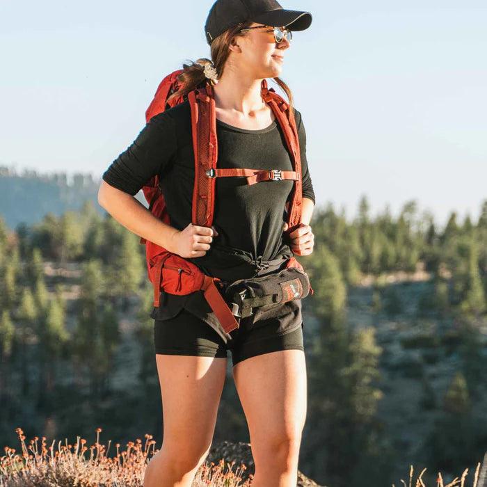 Woman hiking outdoors with a red backpack and black backpacker holster in forest setting