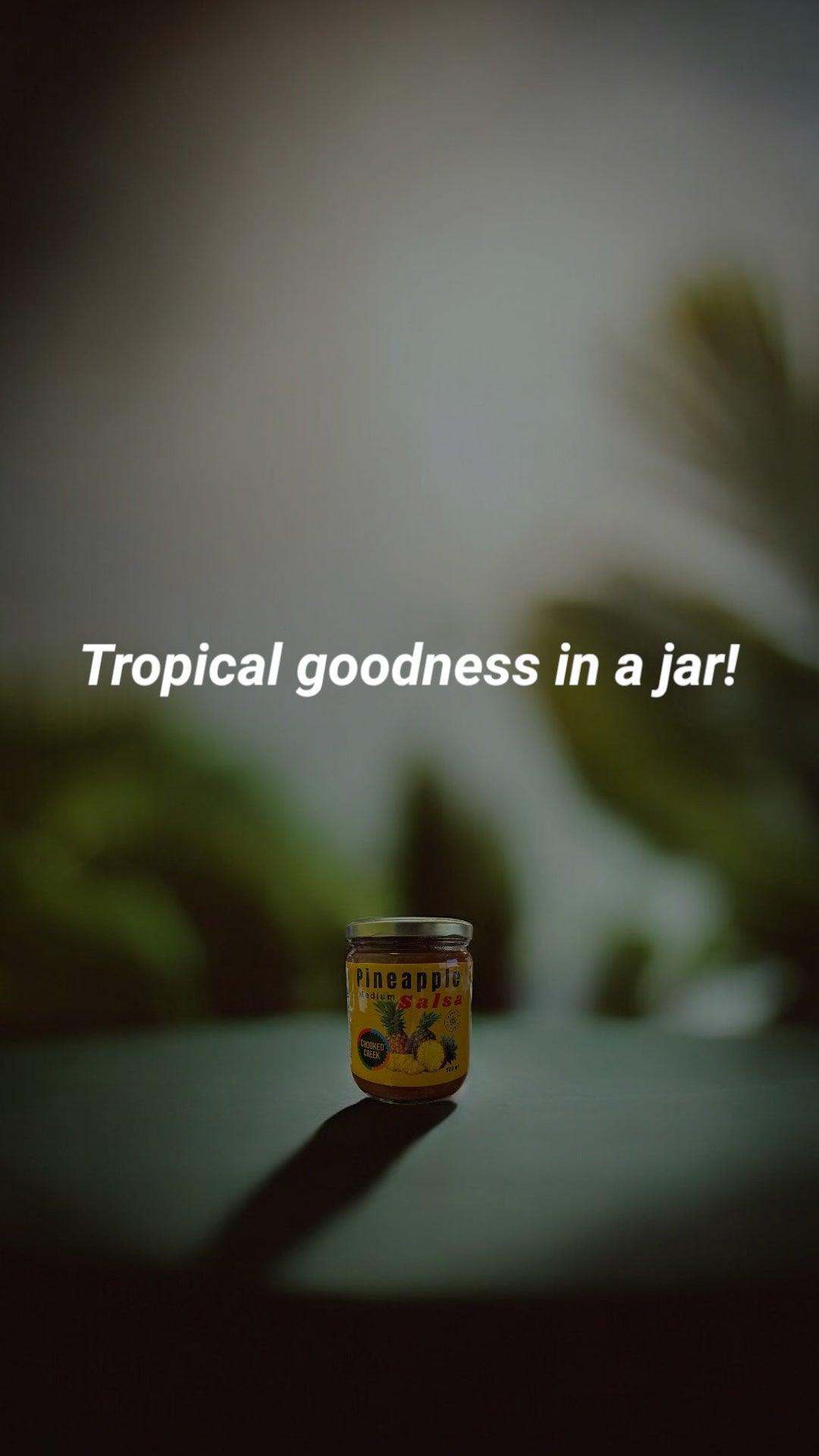 Pineapple salsa jar on dark table, tropical background, 'Tropical goodness in a jar!' text