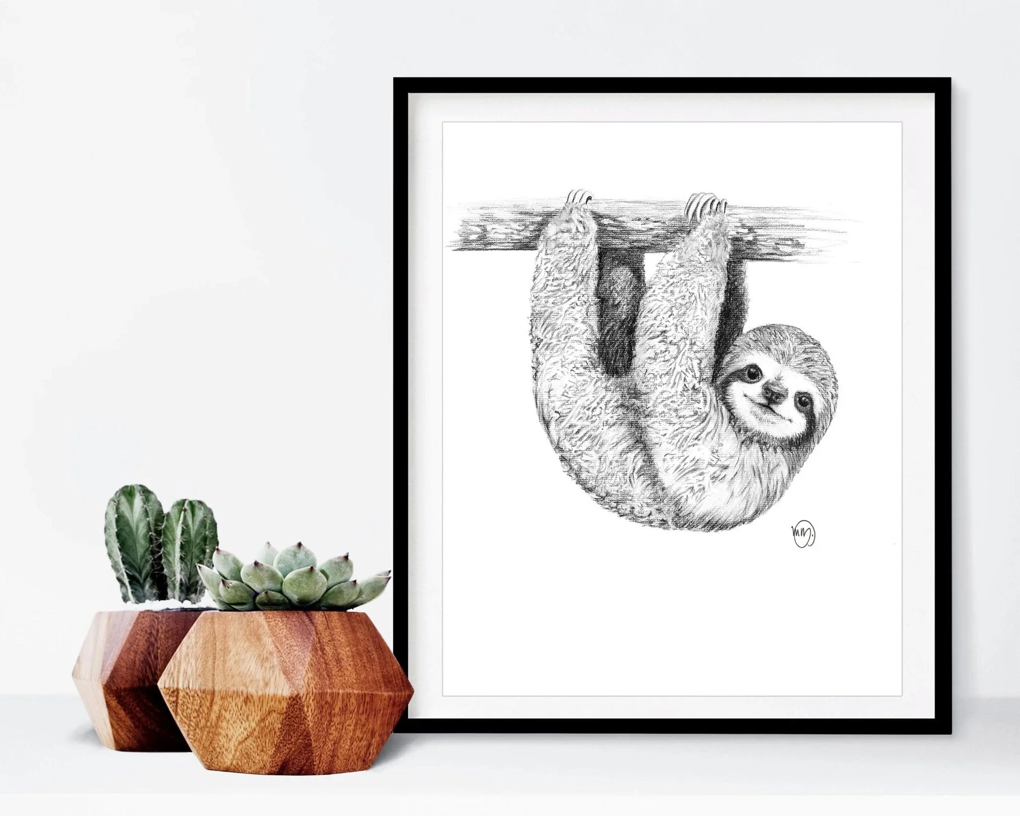 Framed black and white baby sloth art print hanging next to geometric succulent planters