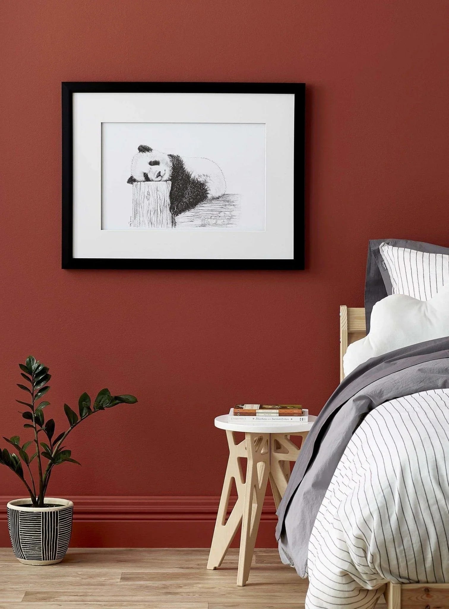Framed sketch of a cute sleeping panda on a red wall above a modern bedroom side table