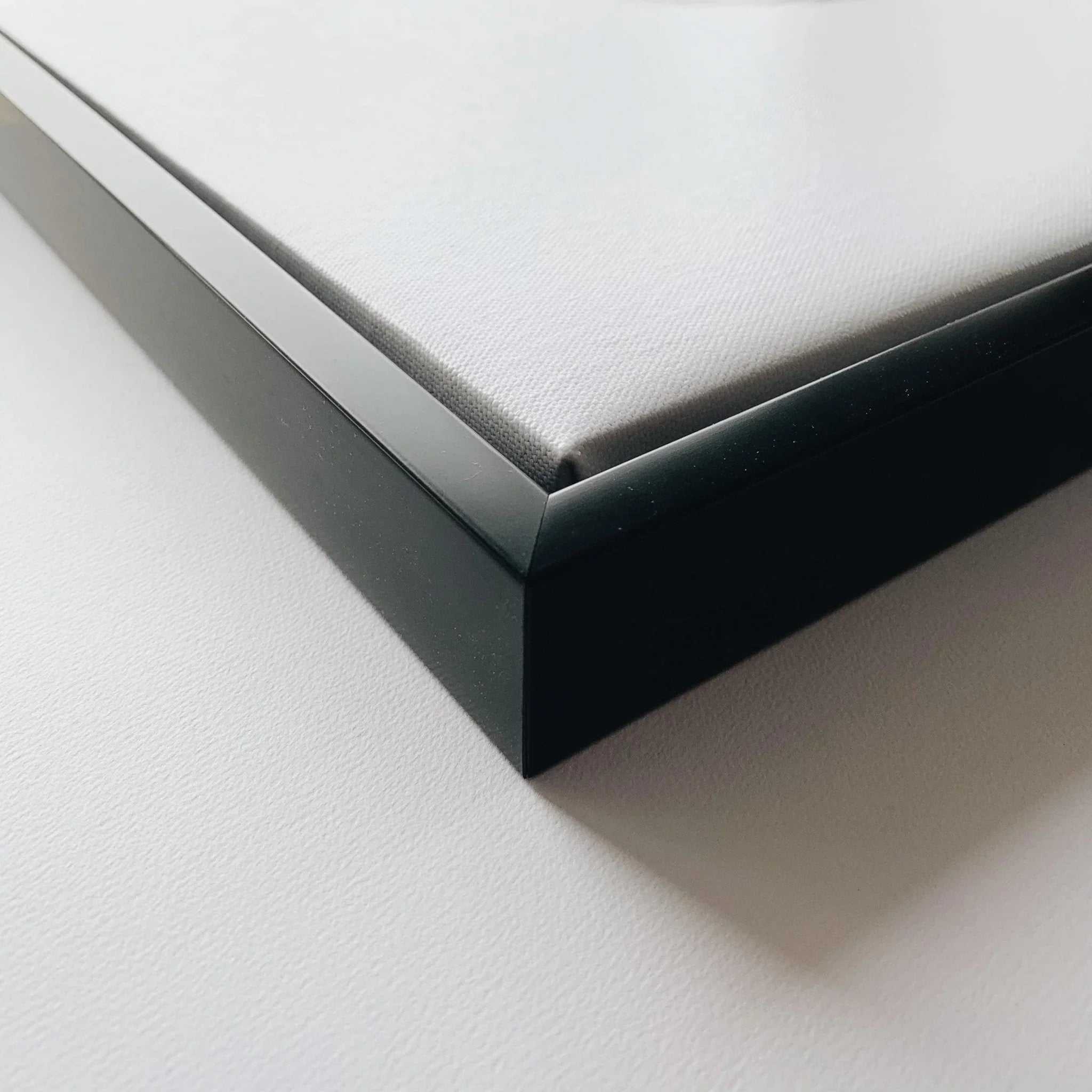 Close-up of a black frame holding a white canvas on a white surface.