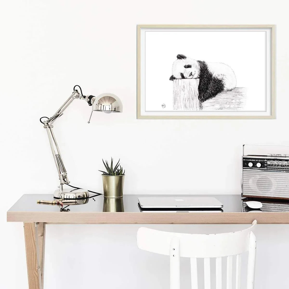 Framed cute sleeping panda drawing hanging above minimalist desk with lamp and plant