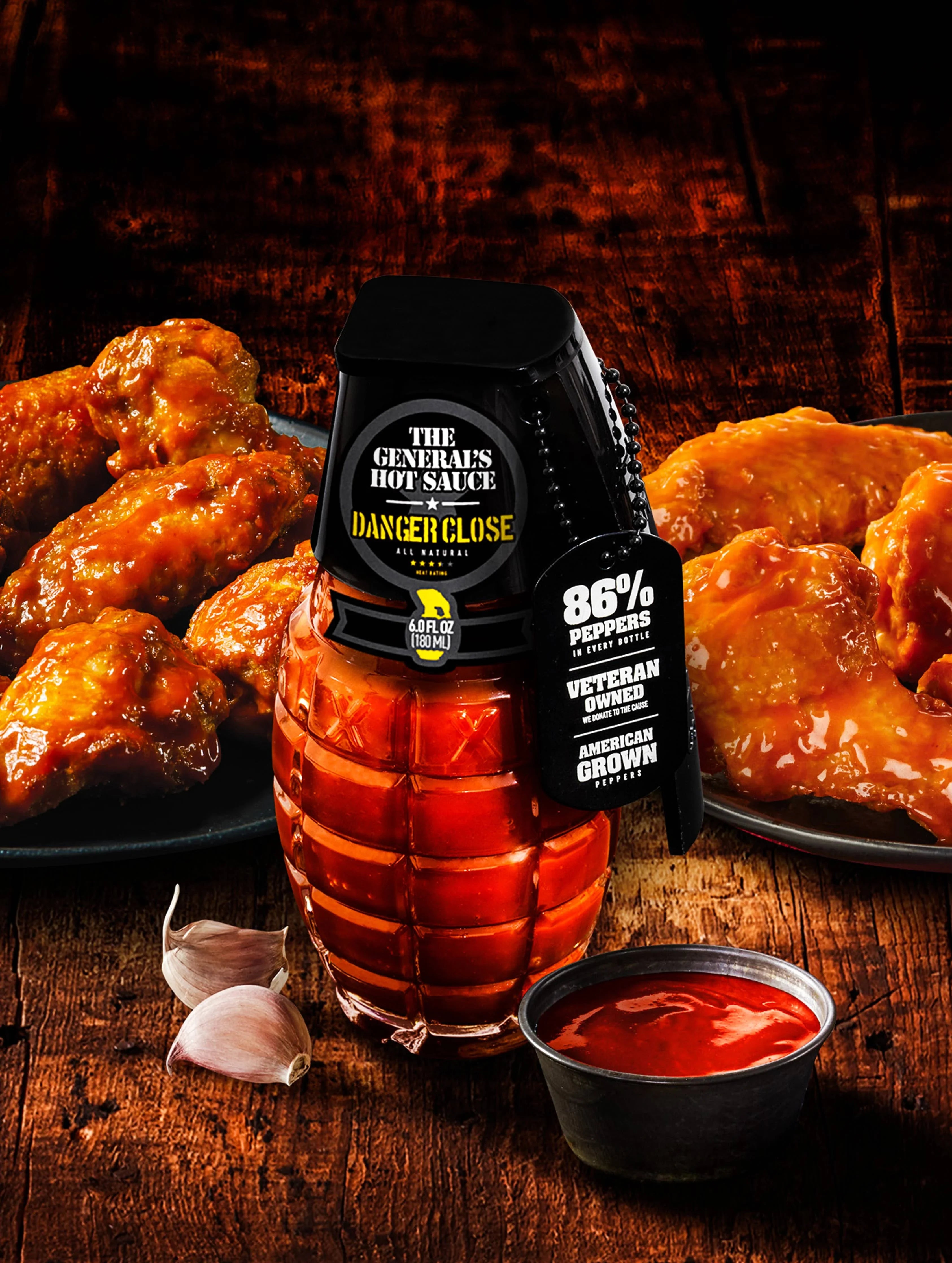 The General's Hot Sauce grenade bottle with buffalo wings, sauce cup, and garlic on rustic table.