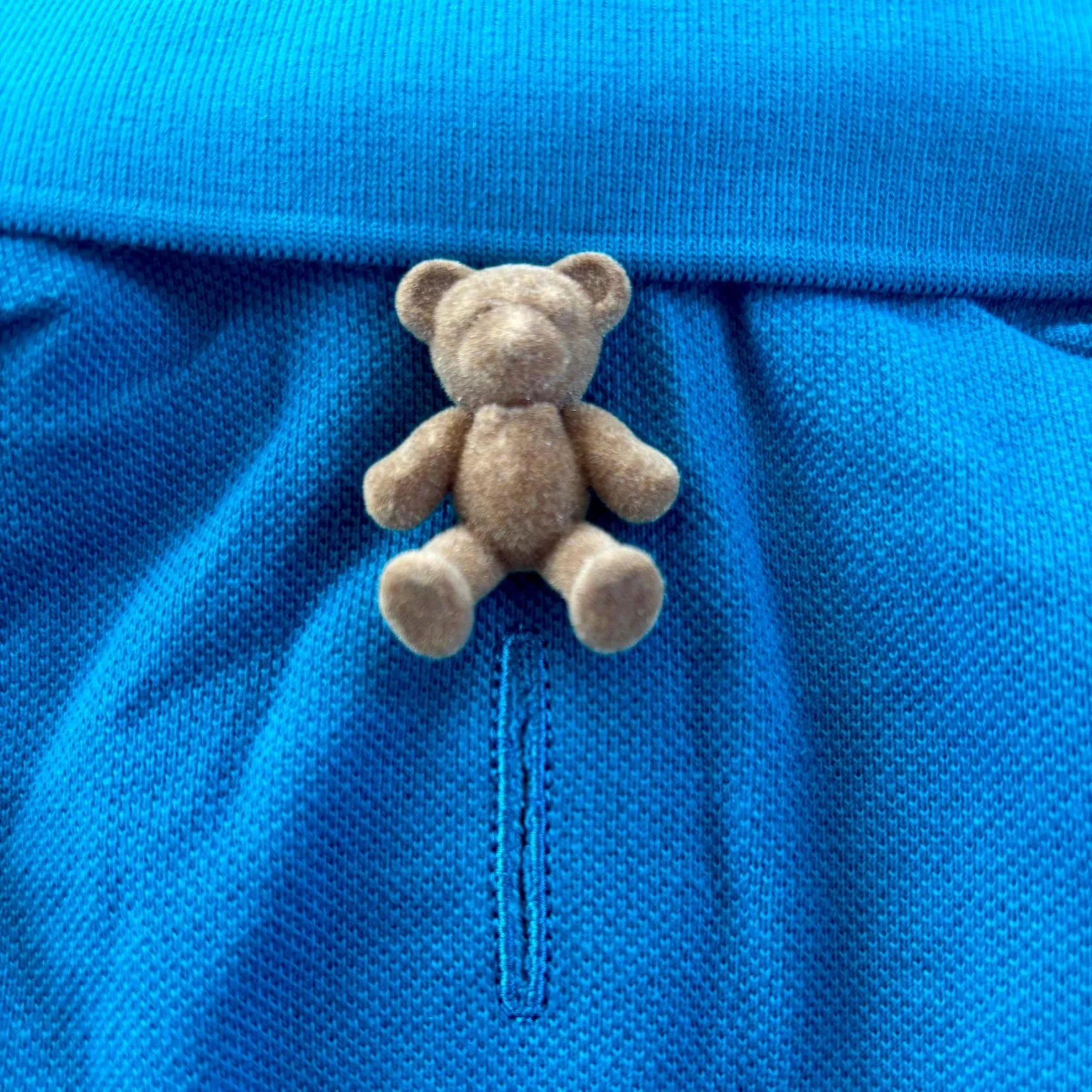 Small brown teddy bear pin on blue textured fabric, cute bear accessory for clothing